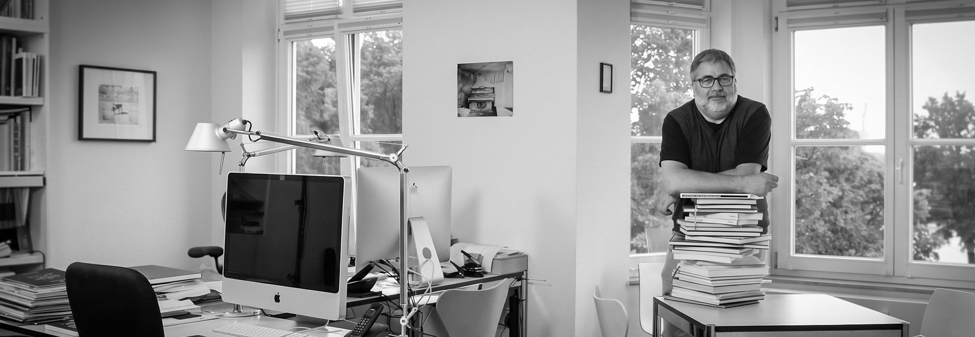 Arne Olsen in seinem Büro, auf einen Stapel eigener Bücher gestützt